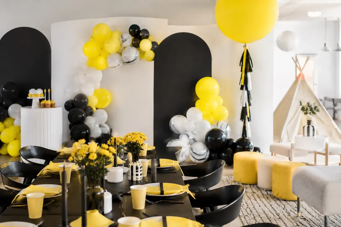 Salón de fiestas decorado en amarillo y negro con globos y mesa dulce